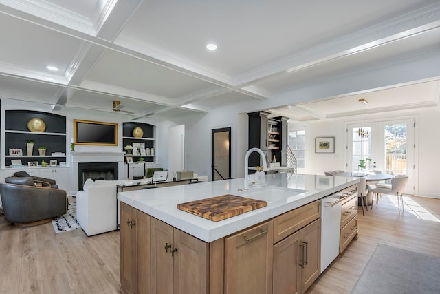 kitchen with beam ceiling, sink, light hardwood / wood-style floors, and a center island with sink