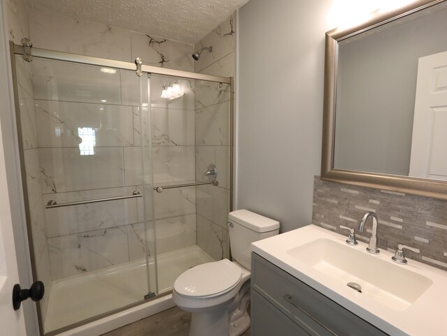 bathroom with an enclosed shower, a textured ceiling, decorative backsplash, toilet, and vanity