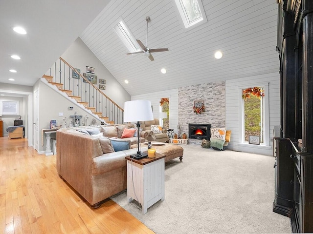 living room featuring high vaulted ceiling, light hardwood / wood-style flooring, a skylight, ceiling fan, and a fireplace