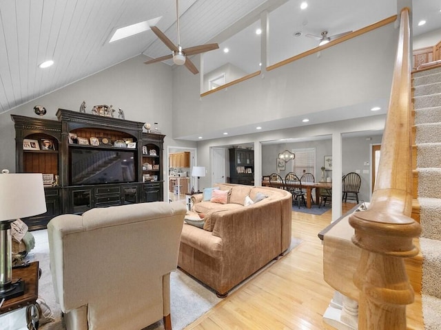 living room with ceiling fan, a skylight, high vaulted ceiling, and light hardwood / wood-style flooring