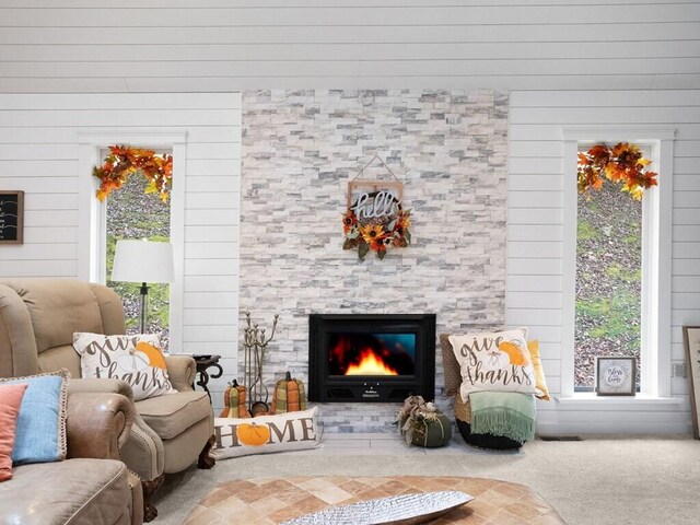 living room featuring a fireplace, wooden walls, plenty of natural light, and carpet floors