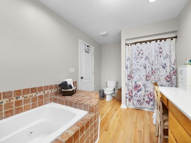 bathroom with hardwood / wood-style flooring, vanity, toilet, and tiled bath