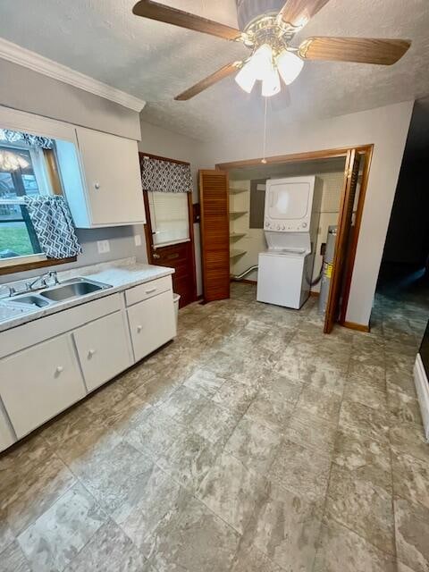 kitchen with white cabinets, ceiling fan, stacked washer and clothes dryer, and sink