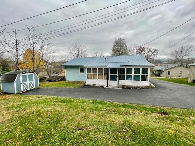 back of house with a lawn, a storage unit, and a sunroom