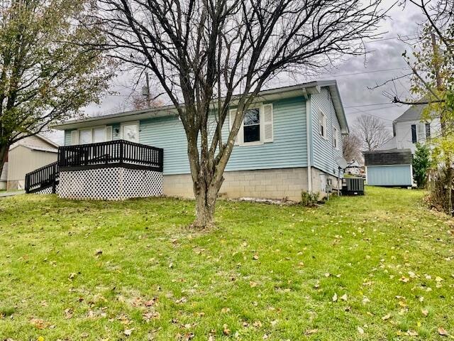 rear view of property featuring a storage shed, a yard, a wooden deck, and central AC