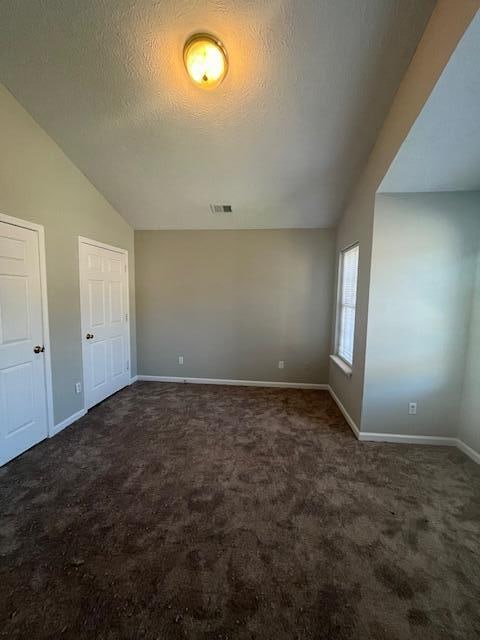 empty room with a textured ceiling, dark carpet, and vaulted ceiling