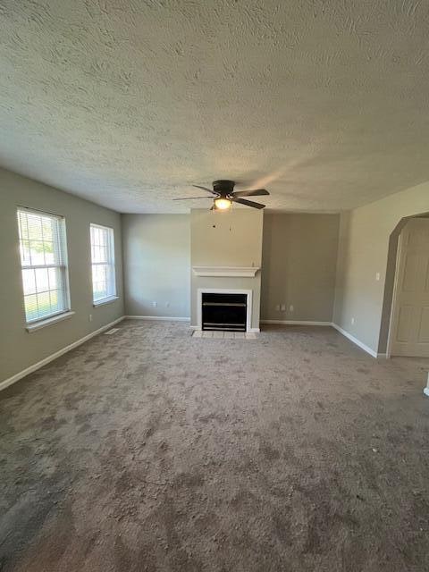 unfurnished living room with a textured ceiling, carpet floors, and ceiling fan