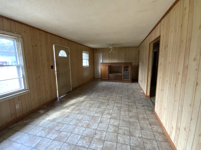 unfurnished living room featuring wooden walls, ceiling fan, and a wealth of natural light