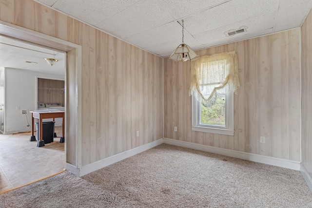 carpeted spare room featuring a chandelier and wood walls