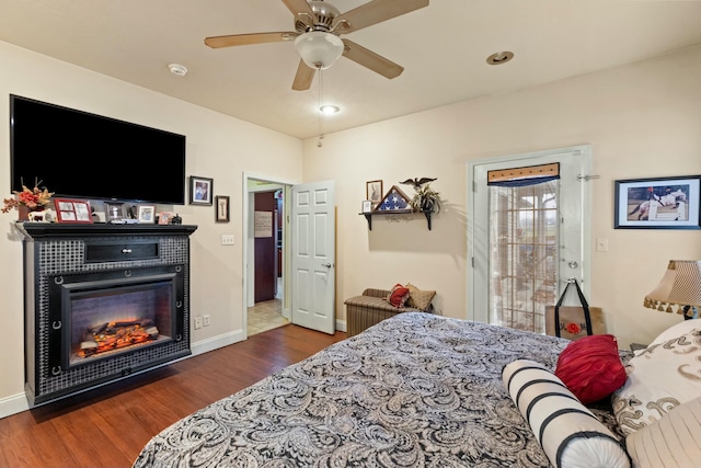 bedroom with dark hardwood / wood-style floors, ceiling fan, and a tiled fireplace