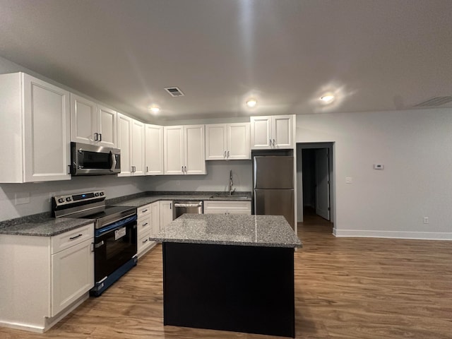 kitchen with stainless steel appliances, sink, hardwood / wood-style floors, a center island, and white cabinetry