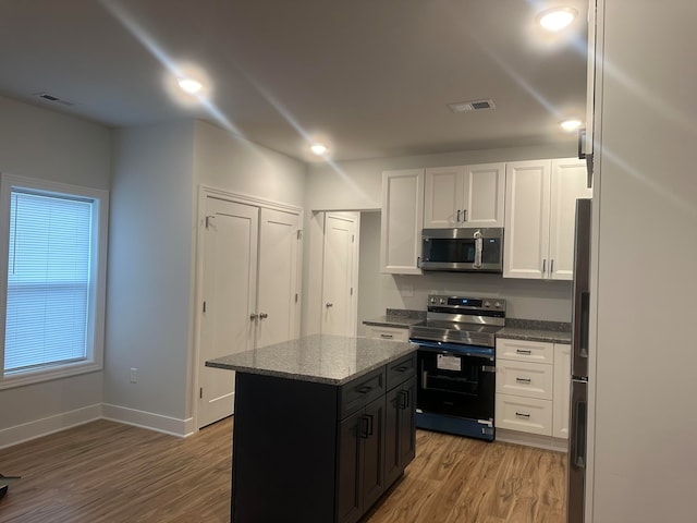 kitchen with light stone countertops, stainless steel appliances, wood-type flooring, white cabinetry, and a kitchen island