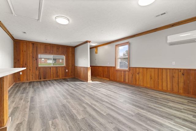 unfurnished living room with crown molding, wooden walls, a textured ceiling, light hardwood / wood-style floors, and a wall unit AC