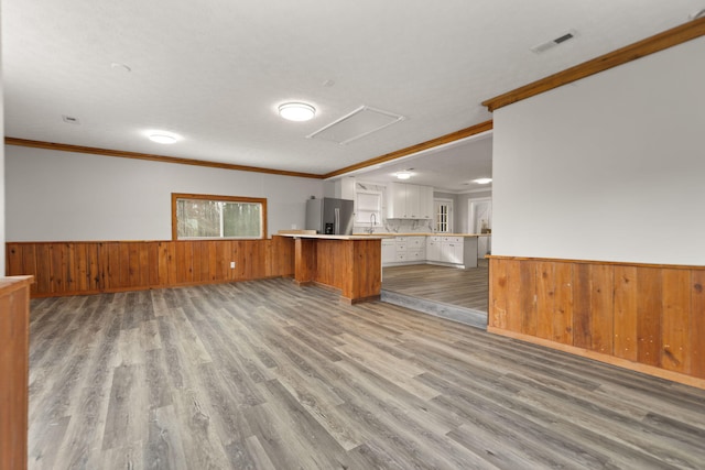 kitchen with kitchen peninsula, stainless steel fridge, crown molding, and light hardwood / wood-style floors