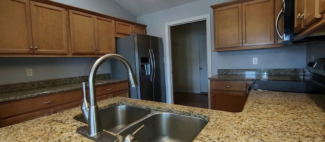 kitchen featuring light stone counters, sink, vaulted ceiling, and appliances with stainless steel finishes