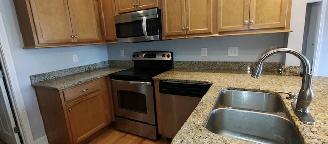 kitchen featuring appliances with stainless steel finishes, light wood-type flooring, light stone counters, and sink