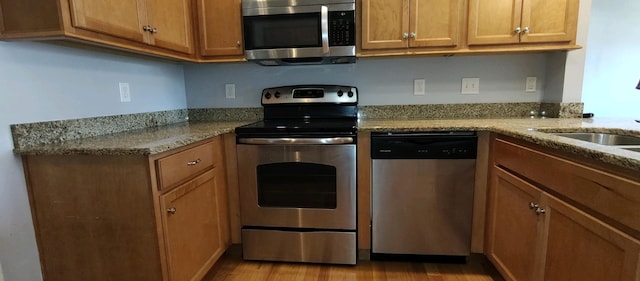 kitchen with light hardwood / wood-style floors, light stone countertops, sink, and appliances with stainless steel finishes