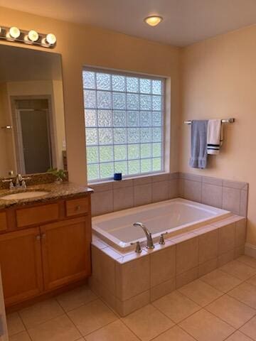 bathroom with tile patterned floors, vanity, a wealth of natural light, and tiled bath