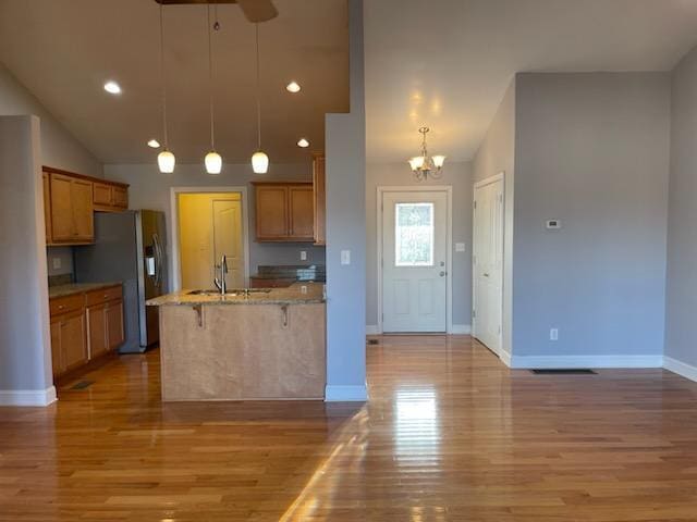 kitchen with stainless steel fridge, light hardwood / wood-style floors, vaulted ceiling, and hanging light fixtures