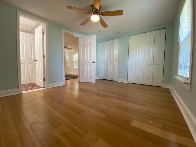 unfurnished bedroom featuring ceiling fan, two closets, and hardwood / wood-style flooring