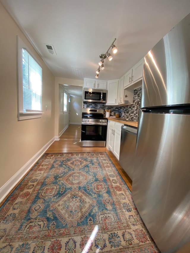 kitchen featuring hardwood / wood-style floors, white cabinetry, appliances with stainless steel finishes, and tasteful backsplash