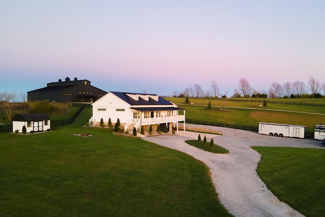 back of house with an outbuilding, curved driveway, fence, a rural view, and a yard