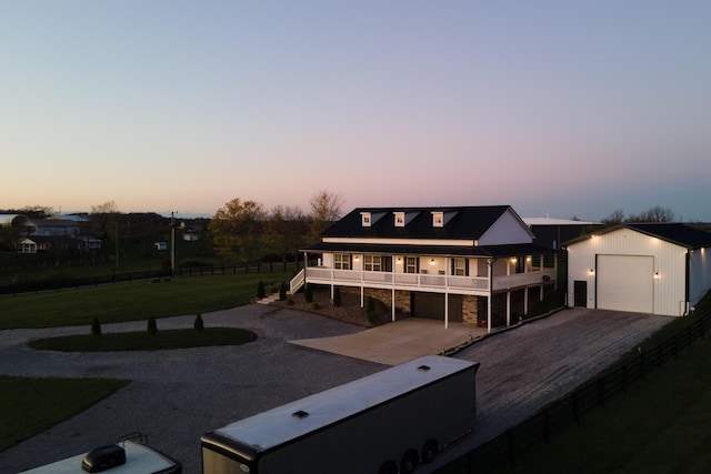 back of property at dusk with stone siding, fence, gravel driveway, a lawn, and an outbuilding