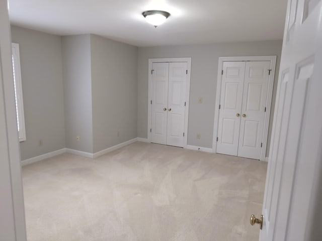 unfurnished bedroom featuring light carpet and multiple closets