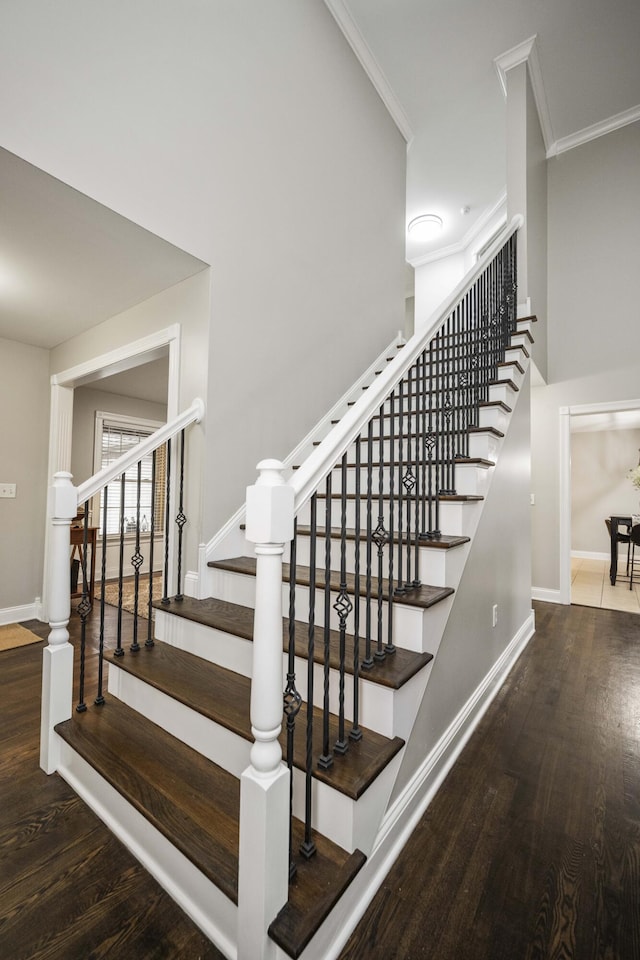 stairway featuring ornamental molding, wood-type flooring, and a high ceiling