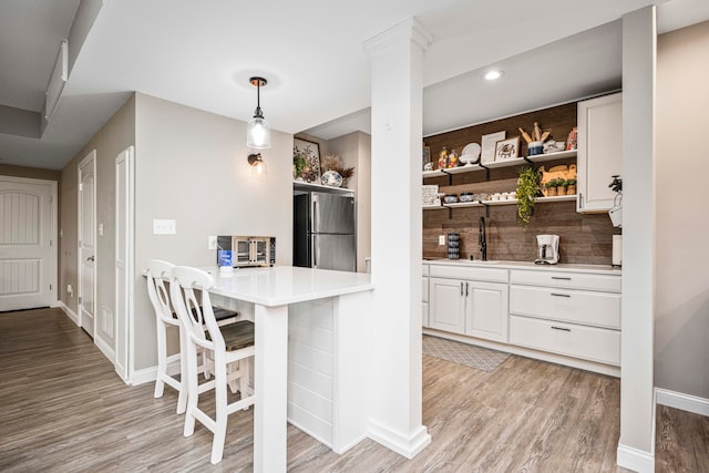 kitchen with pendant lighting, a kitchen breakfast bar, light hardwood / wood-style floors, white cabinetry, and stainless steel refrigerator