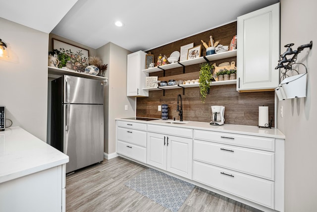 kitchen featuring stainless steel fridge, sink, white cabinets, and light wood-type flooring