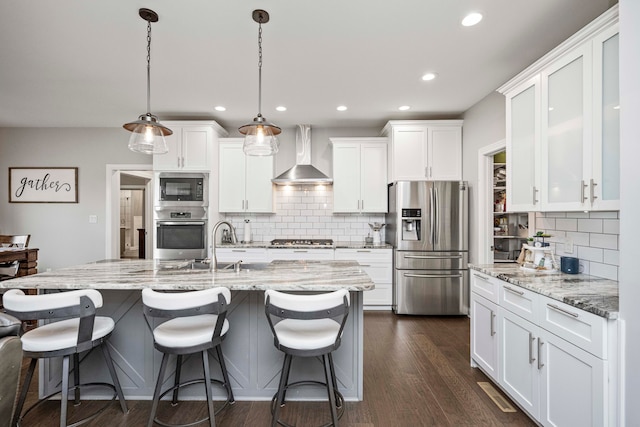 kitchen with white cabinets, wall chimney exhaust hood, stainless steel appliances, and decorative light fixtures