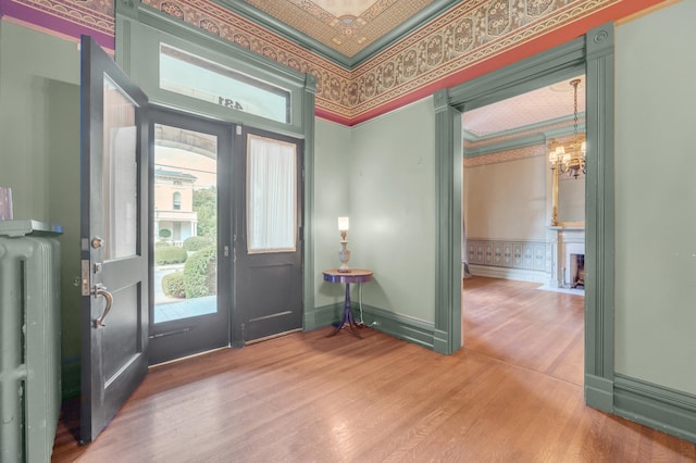 foyer entrance featuring a chandelier, wood-type flooring, radiator heating unit, and crown molding