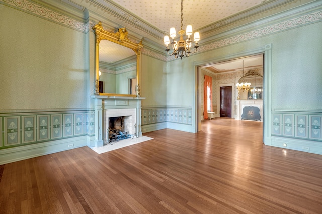 unfurnished living room featuring wood-type flooring, an inviting chandelier, and crown molding