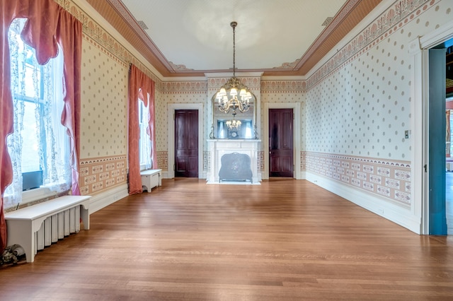 unfurnished living room with a chandelier, a healthy amount of sunlight, light hardwood / wood-style flooring, and crown molding