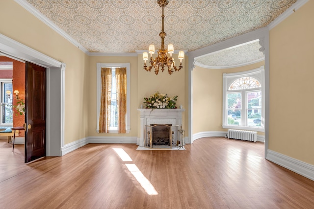 unfurnished living room with crown molding, a tile fireplace, hardwood / wood-style flooring, a notable chandelier, and radiator heating unit