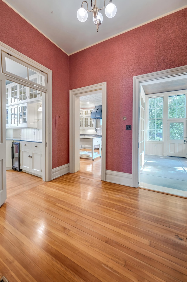 unfurnished dining area featuring a chandelier, light wood-type flooring, and beverage cooler