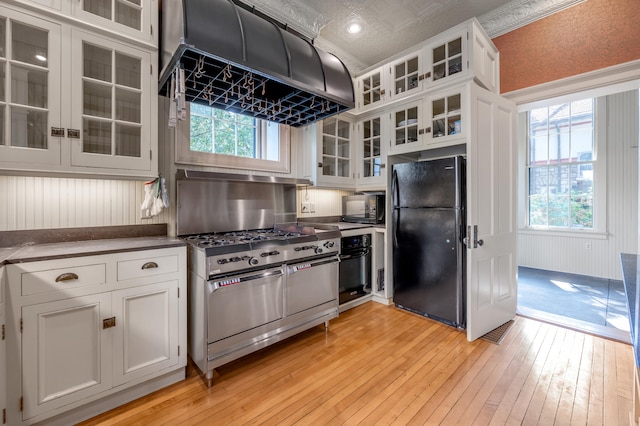 kitchen with black appliances, white cabinets, island exhaust hood, and light hardwood / wood-style flooring