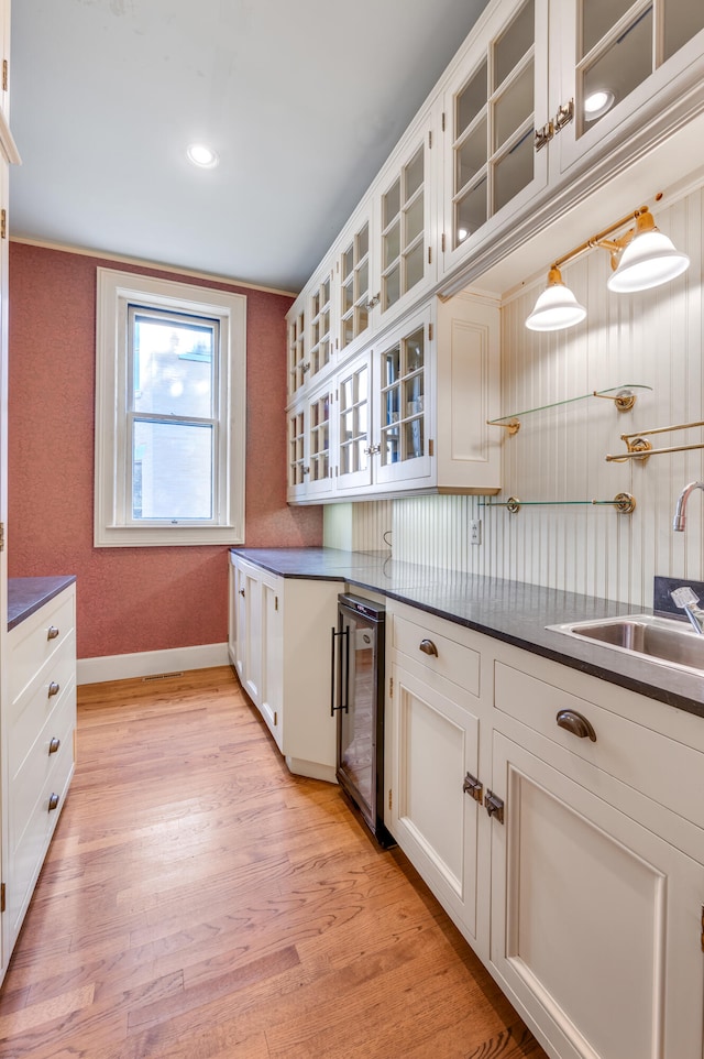 kitchen with light wood-type flooring, beverage cooler, sink, pendant lighting, and white cabinets