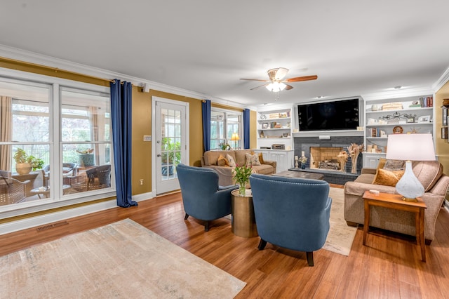 living room featuring built in shelves, ornamental molding, wood-type flooring, and ceiling fan