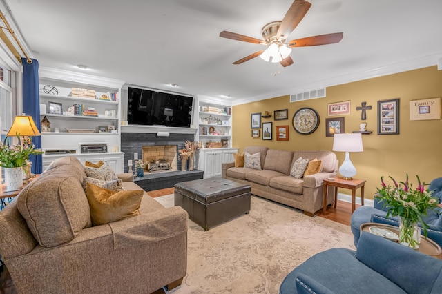 living room with hardwood / wood-style flooring, ceiling fan, ornamental molding, a brick fireplace, and built in shelves