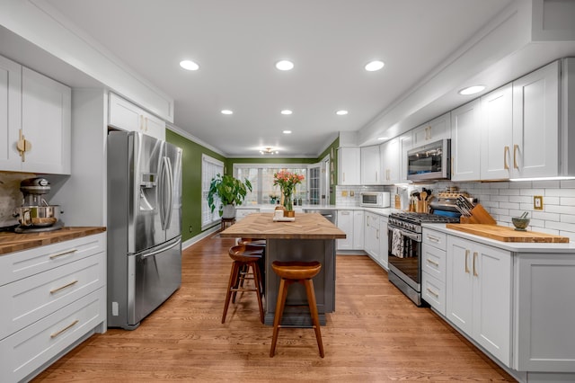 kitchen with butcher block counters, appliances with stainless steel finishes, a kitchen island, decorative backsplash, and white cabinets