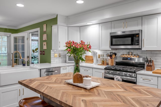 kitchen with sink, appliances with stainless steel finishes, white cabinetry, tasteful backsplash, and ornamental molding