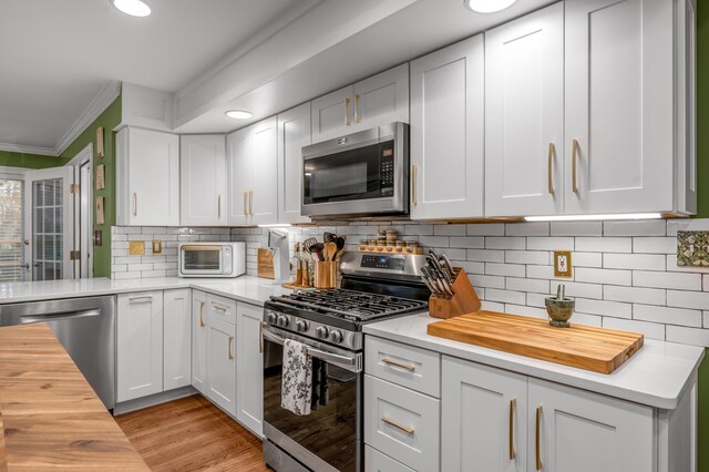 kitchen with tasteful backsplash, appliances with stainless steel finishes, white cabinets, and wood counters