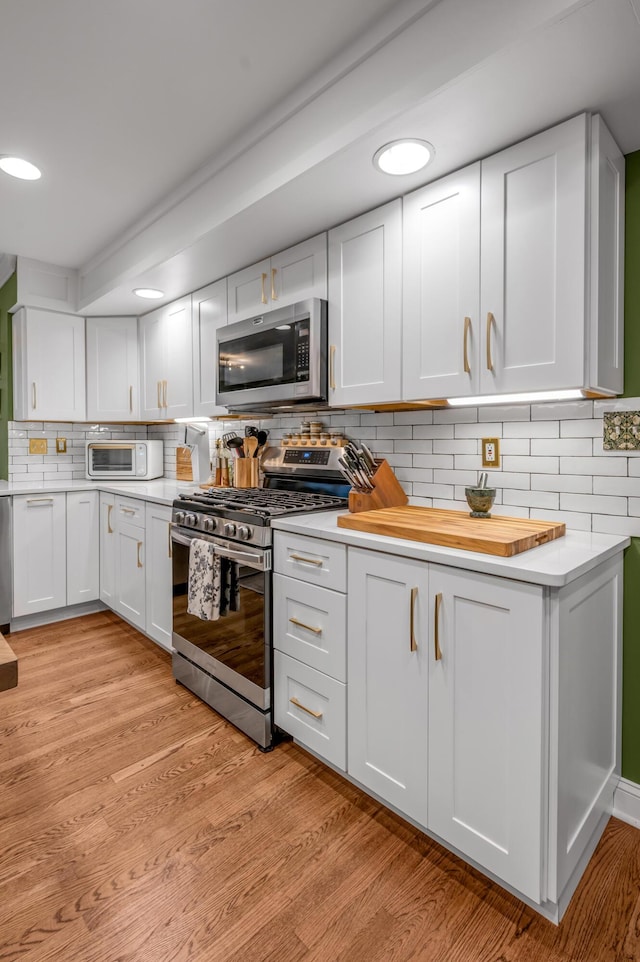 kitchen with tasteful backsplash, stainless steel appliances, light hardwood / wood-style flooring, and white cabinets