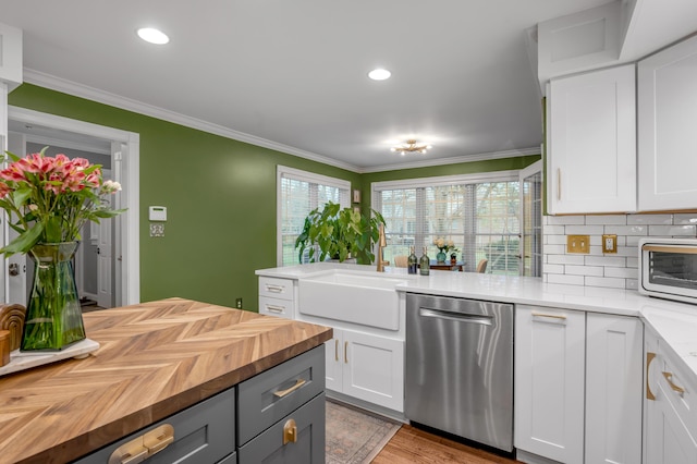 kitchen with butcher block countertops, stainless steel dishwasher, ornamental molding, white cabinets, and backsplash