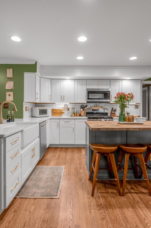 kitchen with wood counters, sink, appliances with stainless steel finishes, a kitchen breakfast bar, and white cabinets