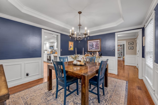 dining space with a notable chandelier, a tray ceiling, light hardwood / wood-style flooring, and ornamental molding