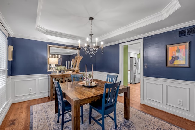 dining space with a raised ceiling, ornamental molding, a notable chandelier, and light hardwood / wood-style floors