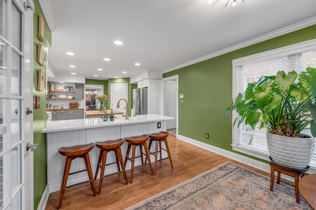 kitchen with a breakfast bar area, light wood-type flooring, stainless steel refrigerator, gray cabinets, and kitchen peninsula